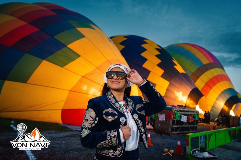 Pasajera con chaqueta bordada mexicana frente a globos aerostáticos iluminados al amanecer