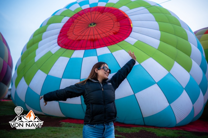 Pasajera celebrando frente a un globo aerostático azul y verde durante el inflado matutino
