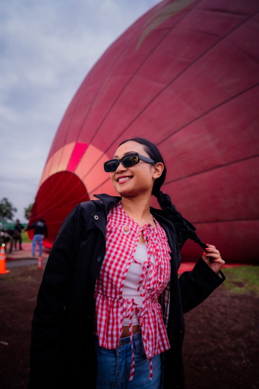 Pasajera sonriente con blusa roja posando frente a un globo aerostático Von Navi antes del despegue