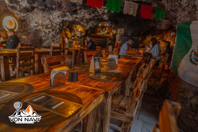 Comedor rústico dentro de una cueva con mesas de madera, bandera mexicana y decoración tradicional